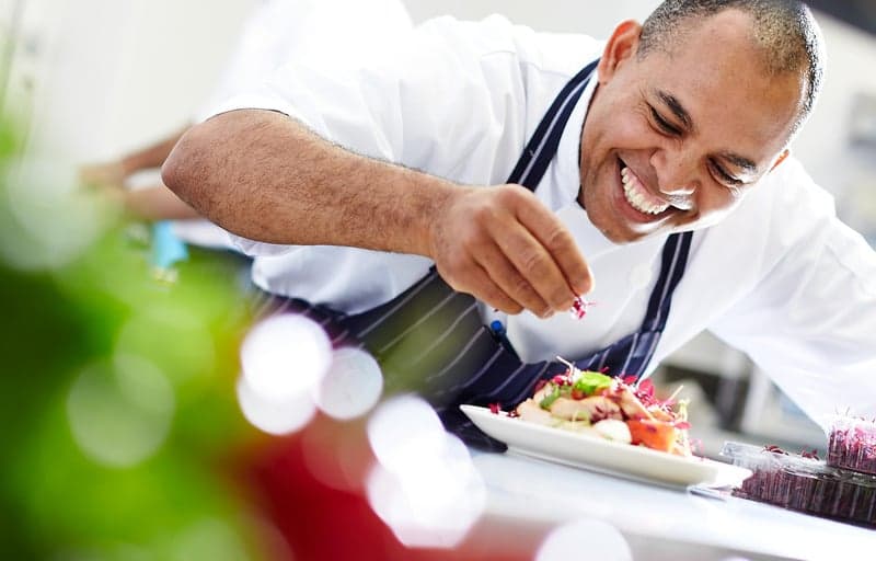 A private chef plating a dish with fresh garnish, candid and mid-motion