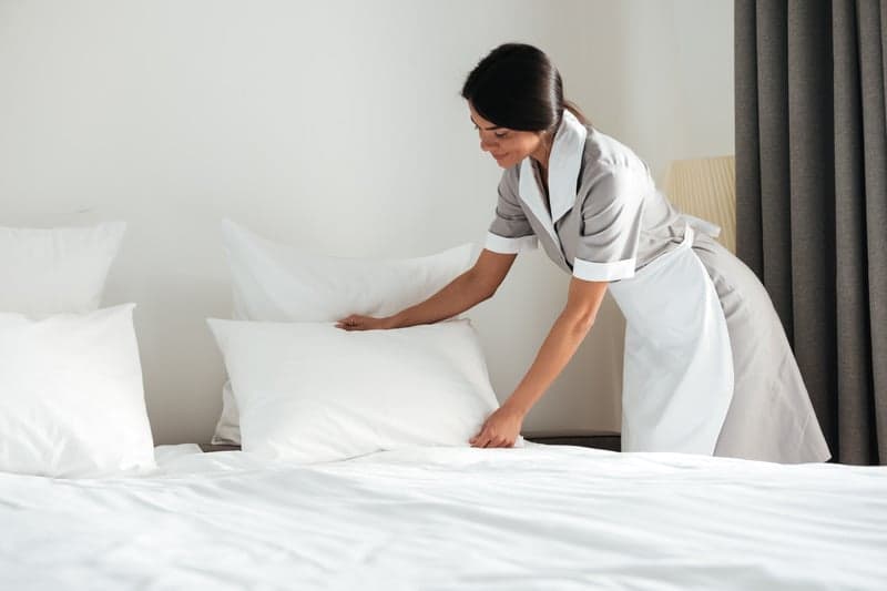 A housekeeper smoothing fresh white bedding in a sunlit bedroom